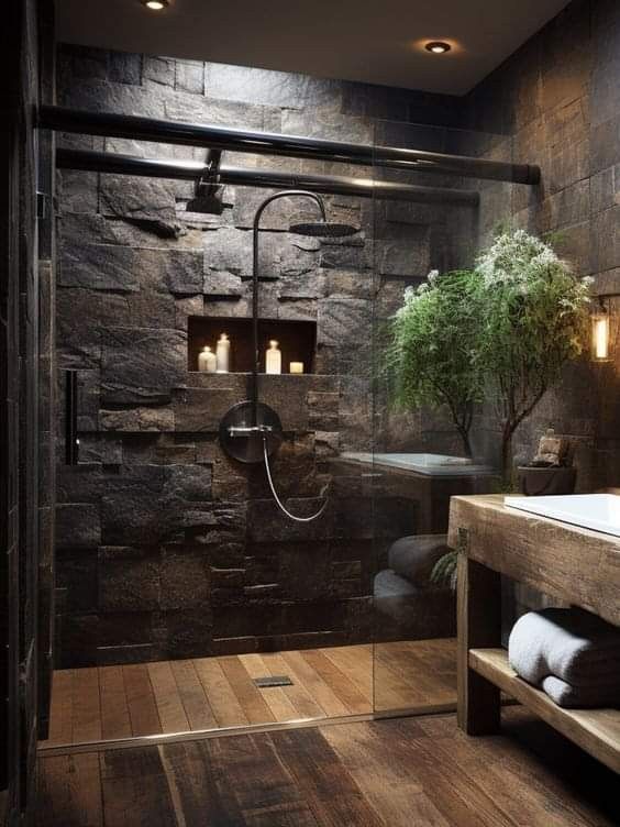 a bathroom with stone walls and wood flooring has a glass shower door that leads to the toilet