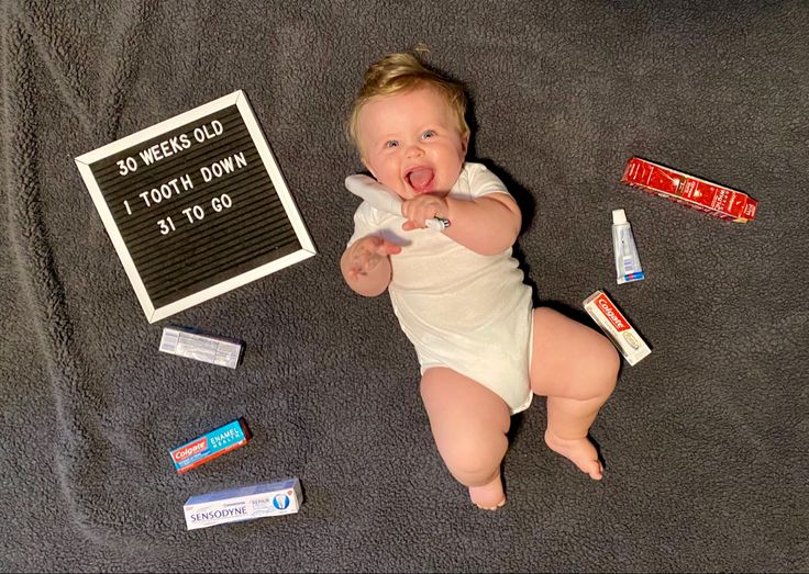 a baby laying on the floor next to some toothpaste