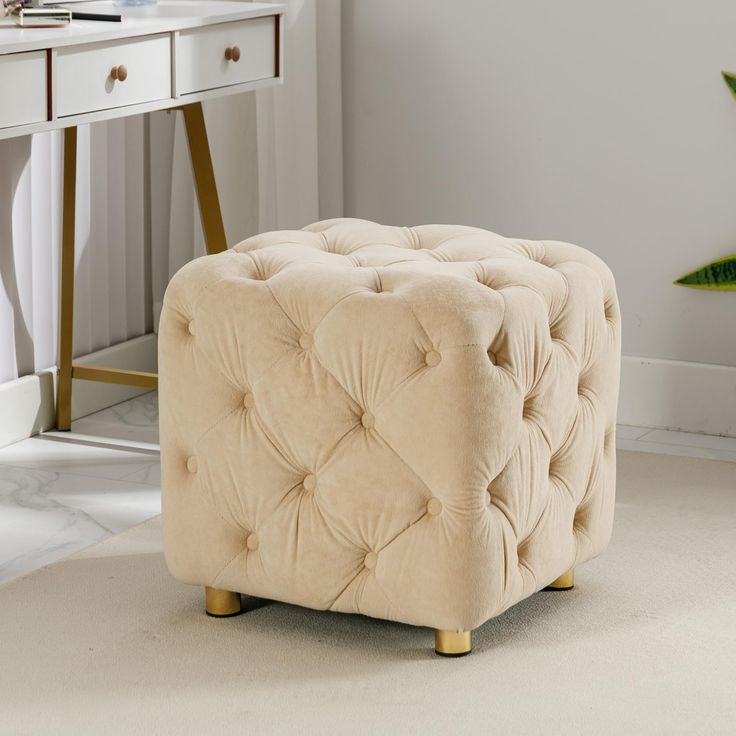 a beige tufted ottoman sits in front of a white desk with a plant on it