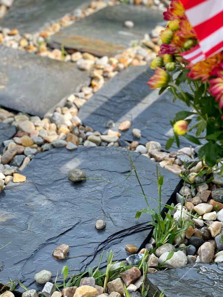 flowers and rocks on the ground with an american flag in the background