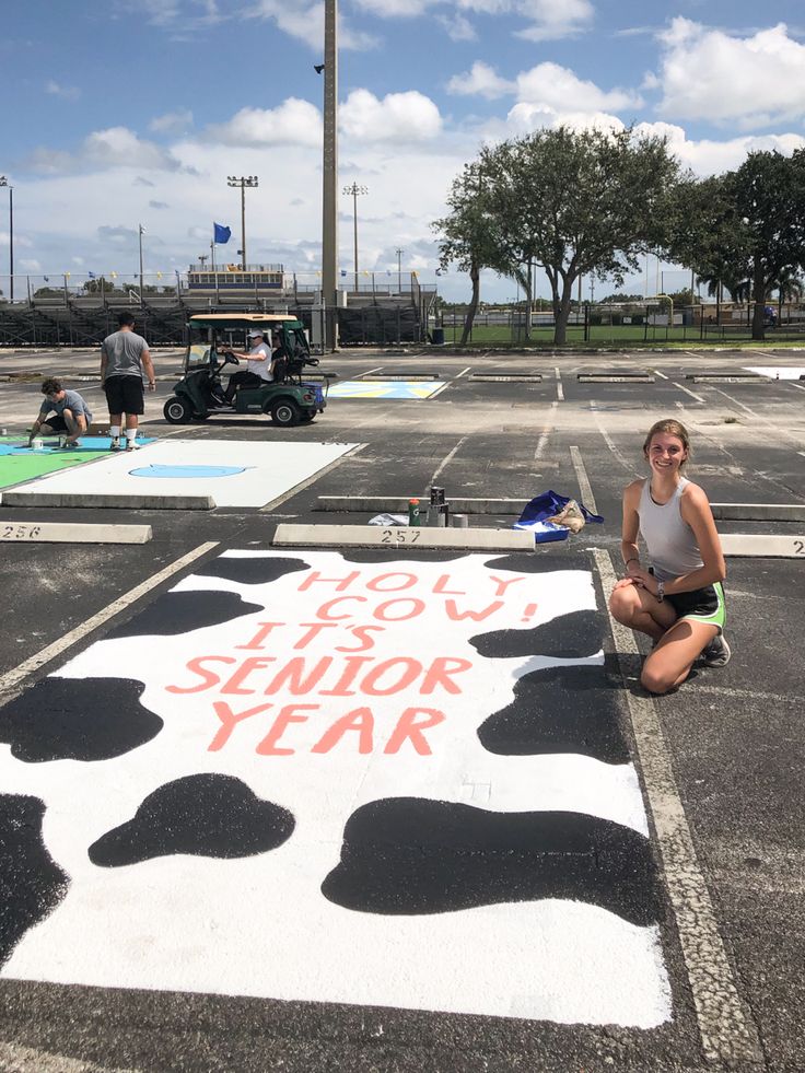 a woman sitting on the ground in front of a painted sign that says, you're an senior year