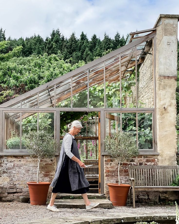 an old woman walking in front of a greenhouse