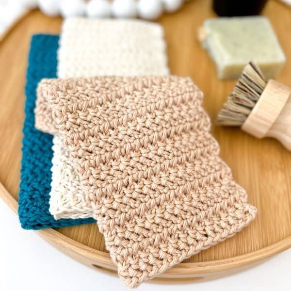 three crocheted dishcloths sitting on top of a wooden plate