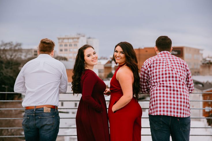 two women in red dresses standing next to three men on a roof with buildings in the background