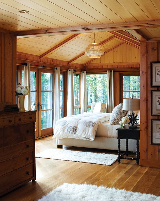 a bedroom with wooden walls and white bedding in the center, along with large windows