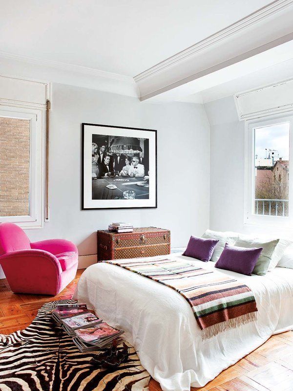 a bedroom with a zebra rug, pink chair and white bed in the corner next to a window