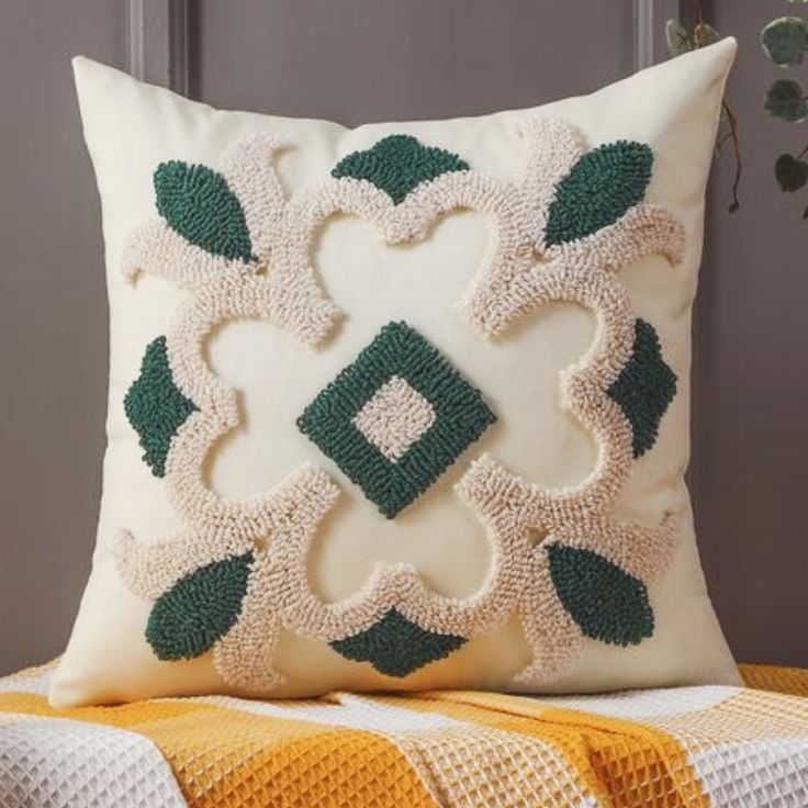 a white and green pillow sitting on top of a couch next to a plant in a vase