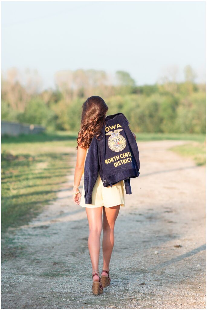 a woman walking down a dirt road with a jacket on her back