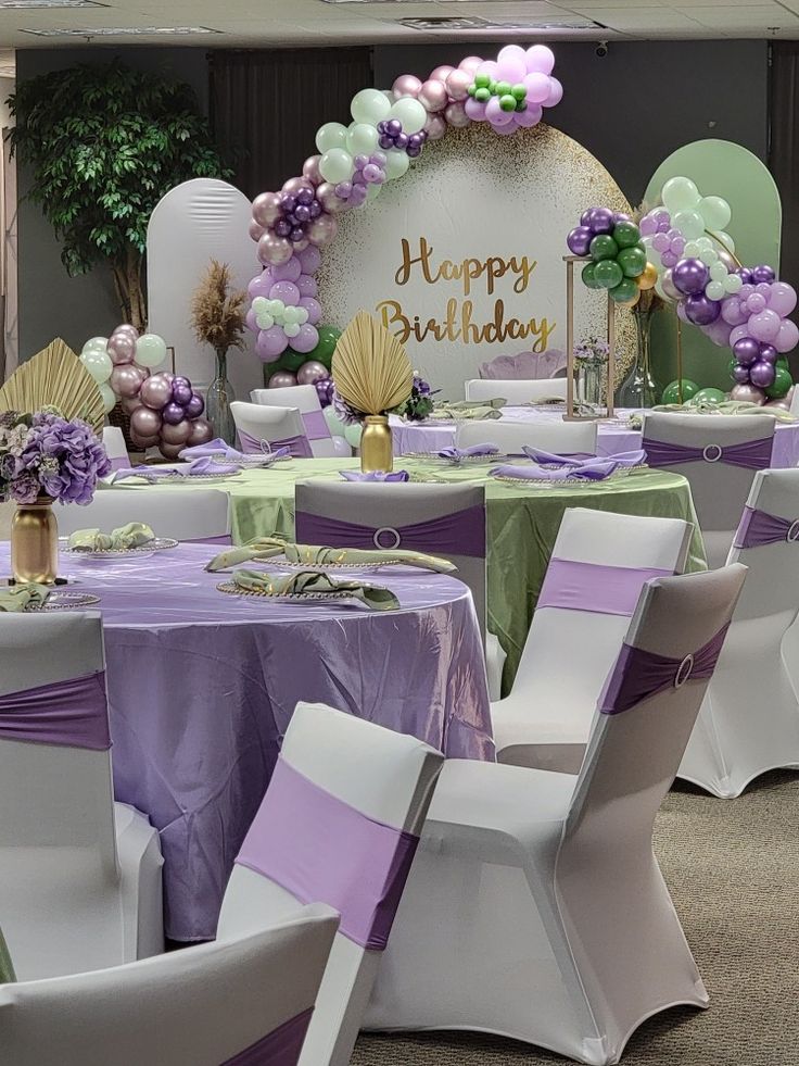 there is a birthday party set up with purple and green decorations on the tables, along with white chairs