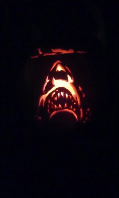 a pumpkin carved to look like a shark with its mouth open and teeth out in the dark