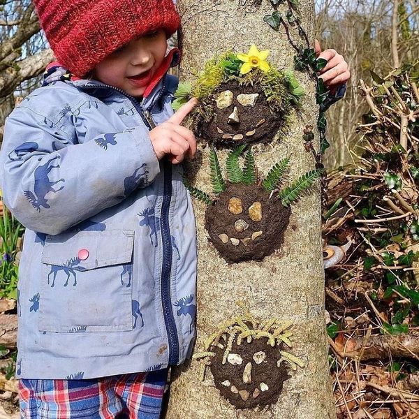 a young boy standing next to a tree with plants and animals painted on the bark