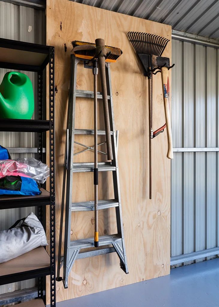 several ladders are hanging on the wall next to shelves with gardening tools and other items