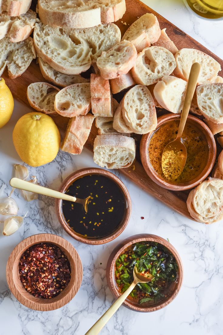 breads and condiments are arranged on a marble counter top with lemons in the background