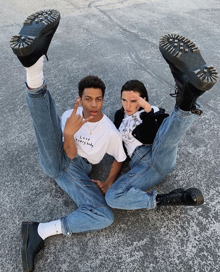 a man and woman sitting on the ground with their feet up in the air, both wearing black shoes