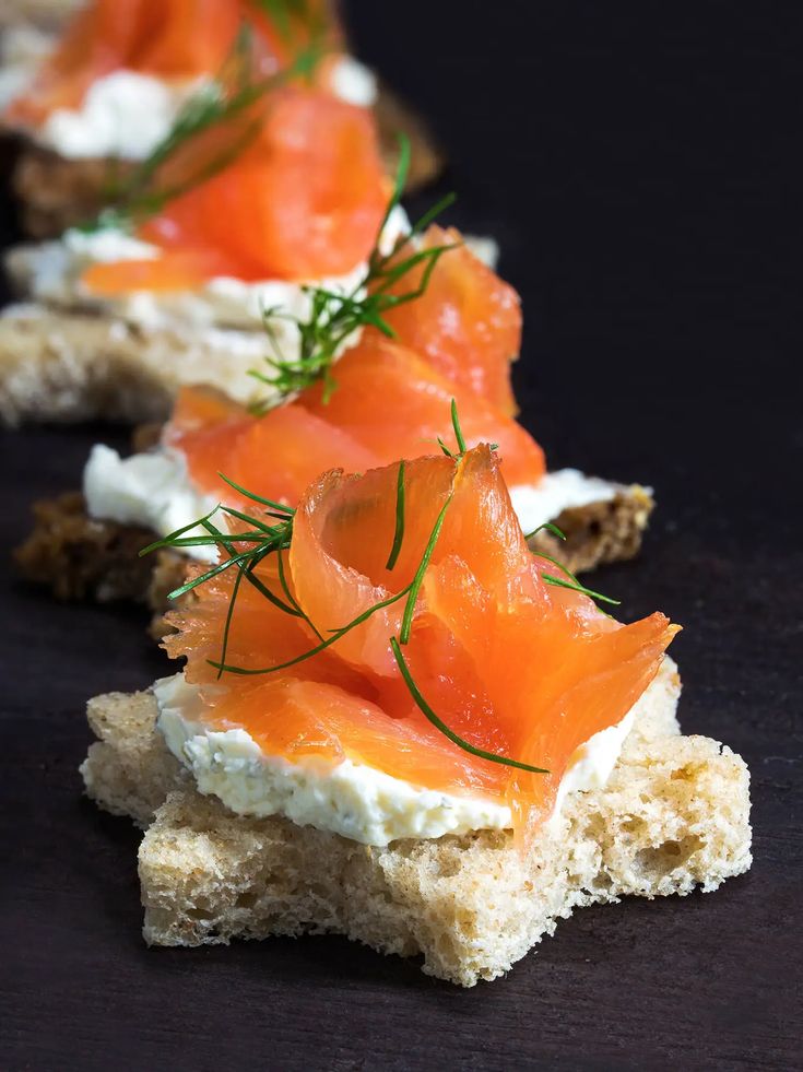 small crackers with smoked salmon and cream cheese on them are arranged on a black surface