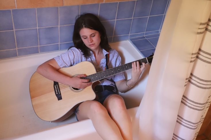 a woman sitting in a bathtub playing an acoustic guitar