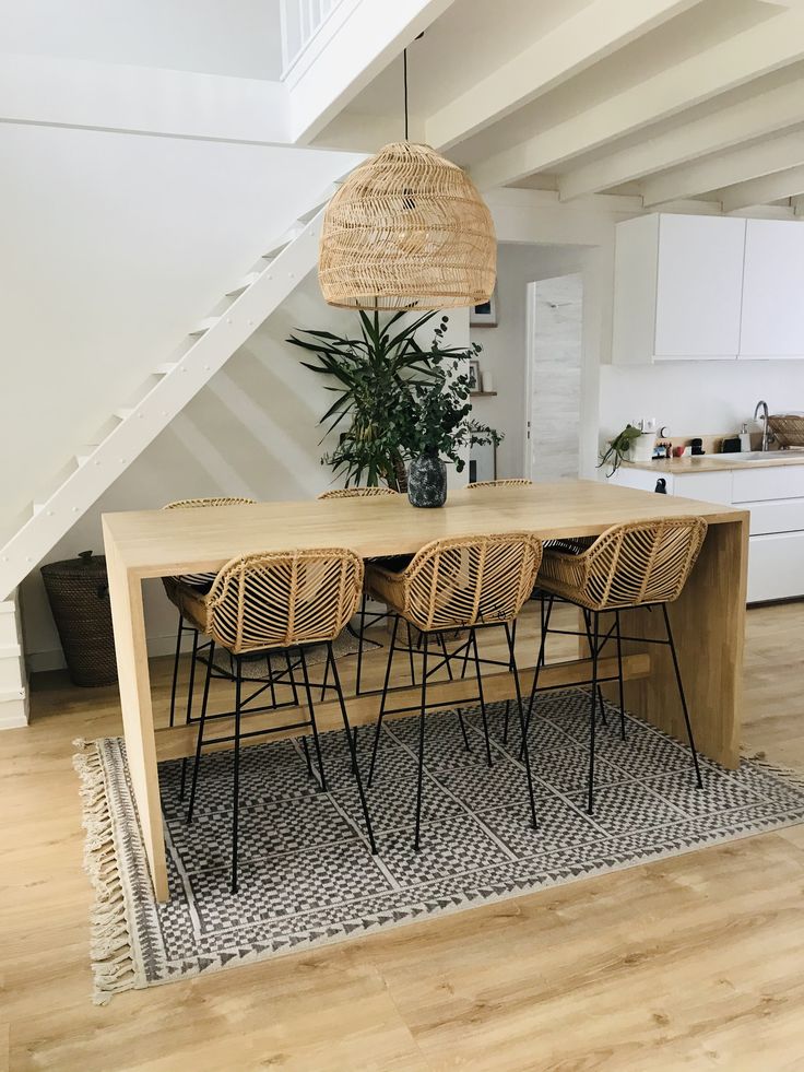 a dining room table with four chairs and a plant in the center, under a stair case