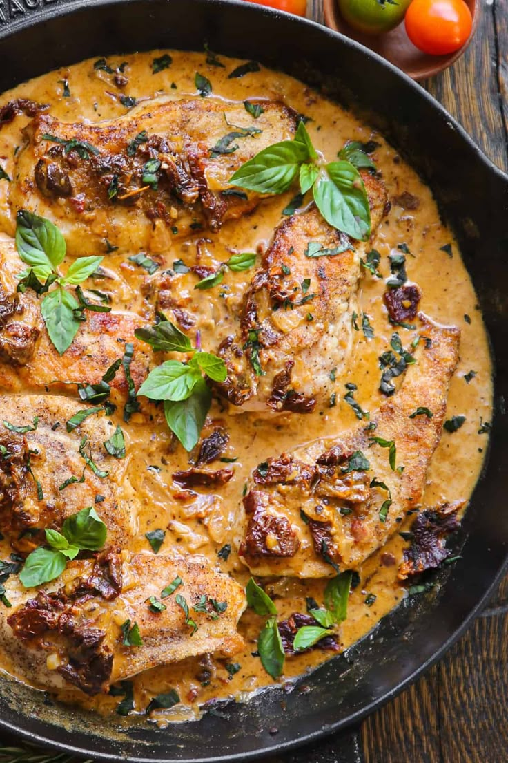 a pan filled with meat covered in sauce and garnished with herbs