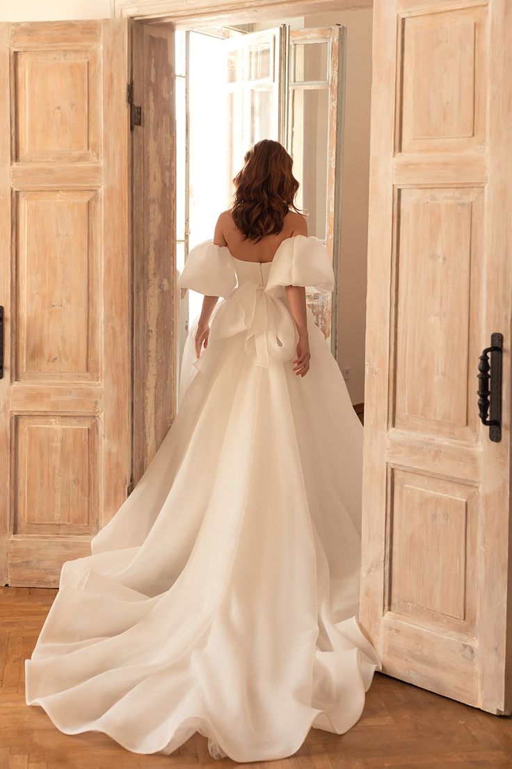 a woman in a white wedding dress is looking into an open door with her back to the camera