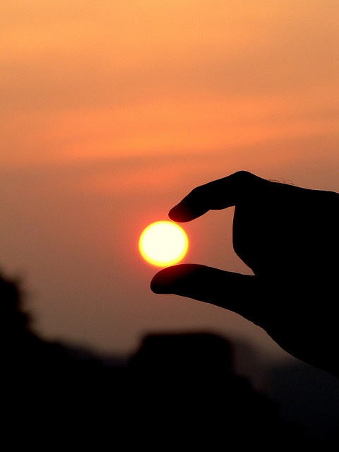 the sun is setting in the sky behind a person holding their hand out to touch it