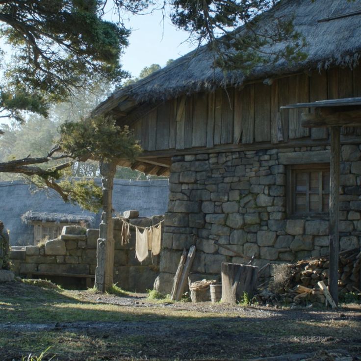 an old stone house with a thatched roof and trees in the foreground on a sunny day