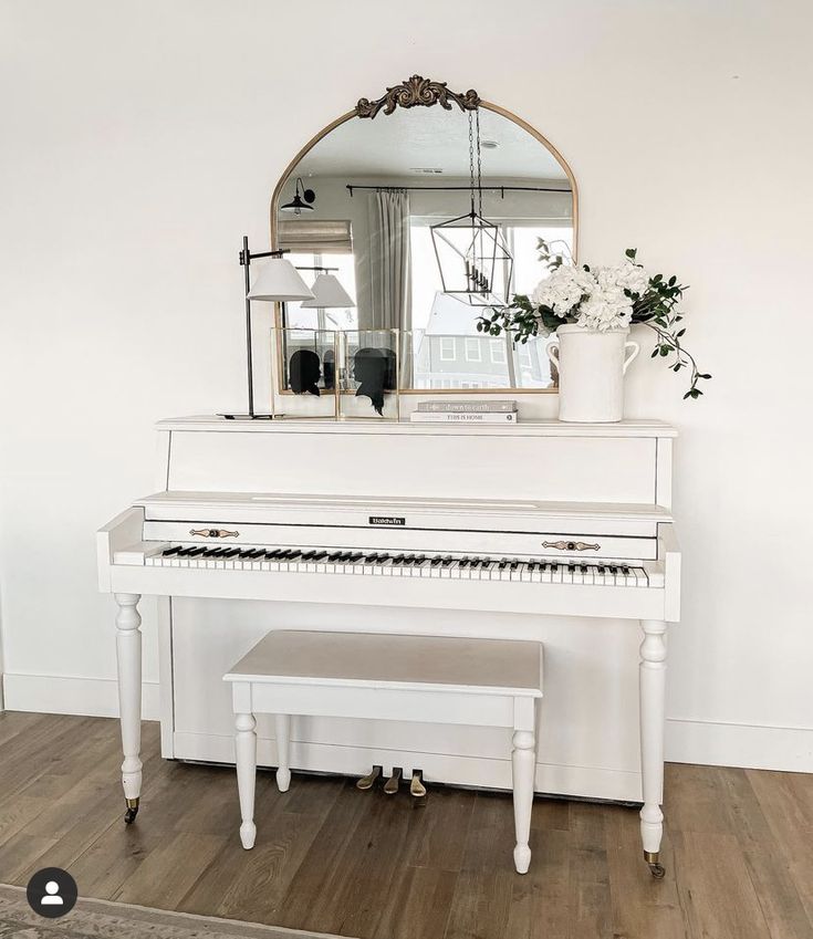 a white piano sitting on top of a hard wood floor next to a vase with flowers