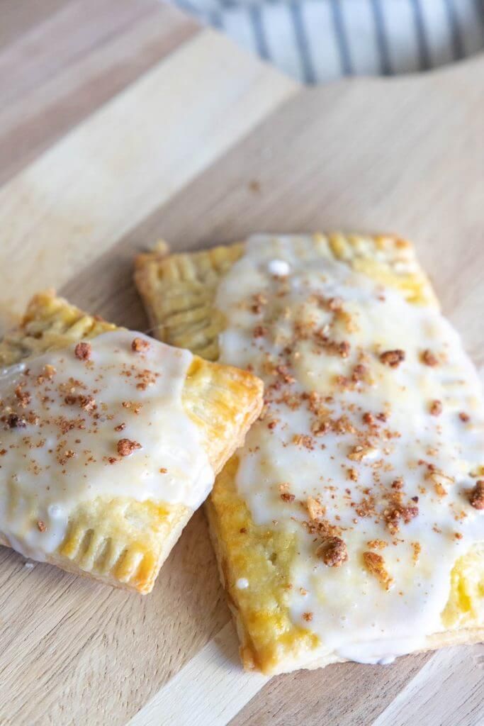 three pastries on a cutting board with white icing and cinnamon sprinkles