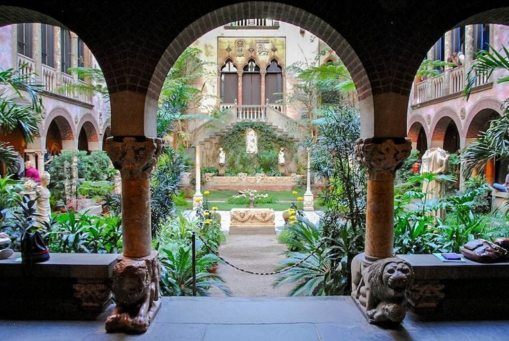 an archway leading into a courtyard with statues and plants in the foreground on either side