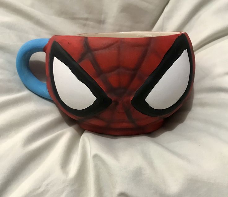 a spider - man mug is sitting on a bed with white sheets and blue handles