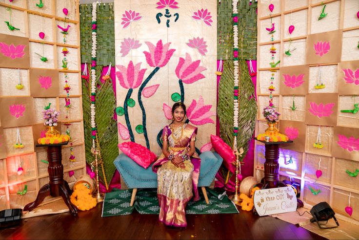 a woman sitting on a blue chair in front of a wall with flowers painted on it