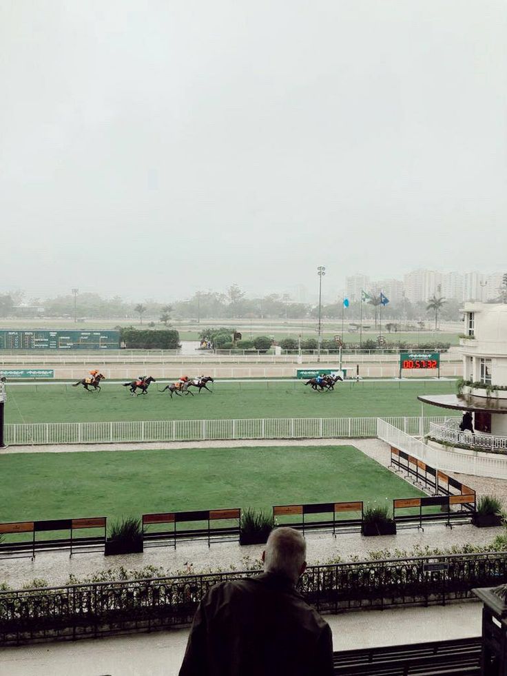 a man is looking at horses running on the track in front of a building and grass field