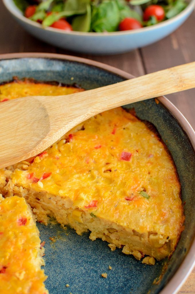 an omelet in a skillet with a wooden spoon on the side next to a salad