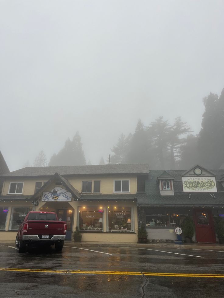 a red truck parked in front of a building on a foggy day with mountains in the background