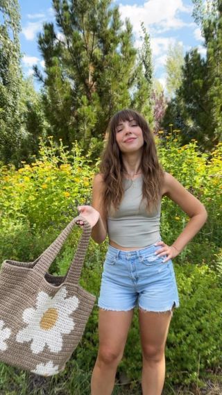 a woman standing in front of flowers holding a purse