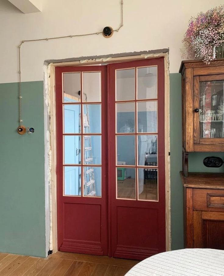 a room with two red doors and a wooden dresser next to the door that has glass panes on it