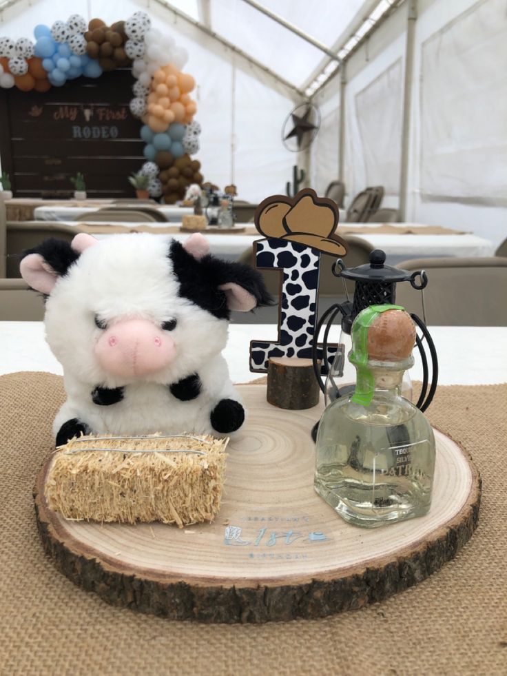 a stuffed cow sitting on top of a piece of wood next to a glass bottle