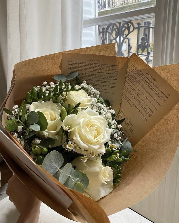 a bouquet of white roses sitting on top of a table next to an open book