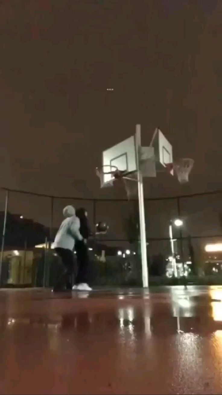 two people are playing basketball on the court at night with lights shining in the background