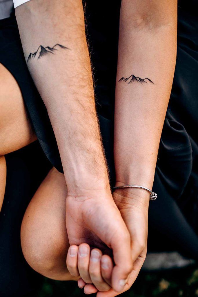 two people holding hands with mountains tattooed on their arm and the other hand behind them