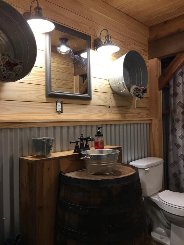 a bathroom with a sink, toilet and wooden barrel in the corner next to a mirror