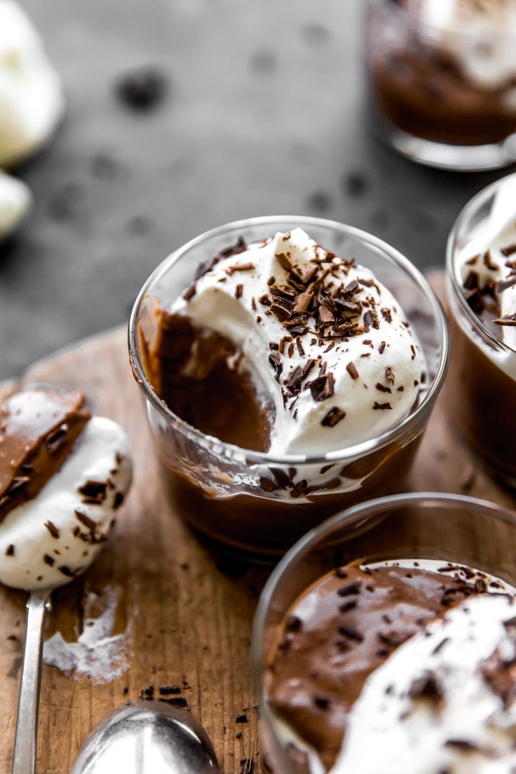 three desserts with chocolate and whipped cream in small glasses on a wooden board next to spoons