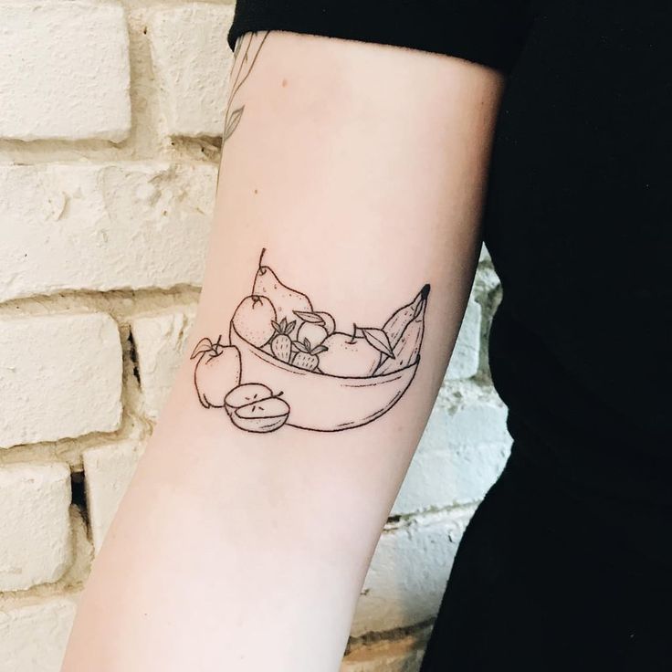 a woman with a tattoo on her arm has a bowl of fruit and an apple