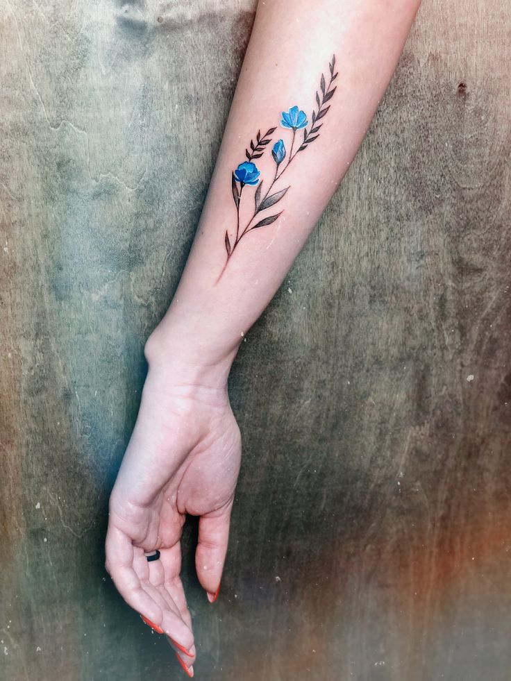 a woman's arm with a blue flower tattoo on her left forearm and hand