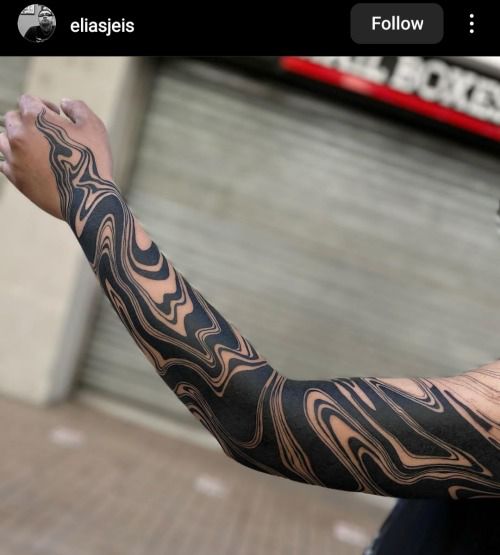 a man's arm with black and grey tattoos on it, in front of a building