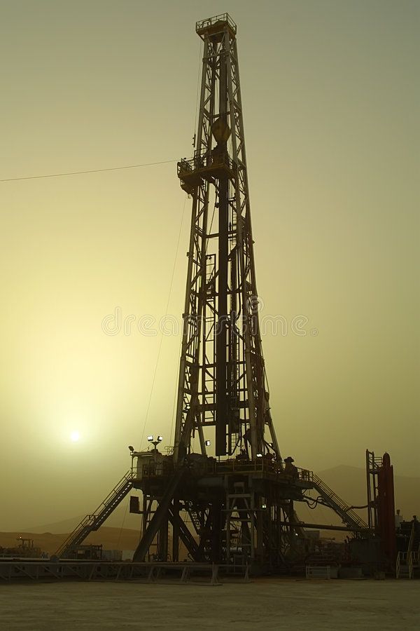 an oil rig sitting in the middle of a field with the sun setting behind it