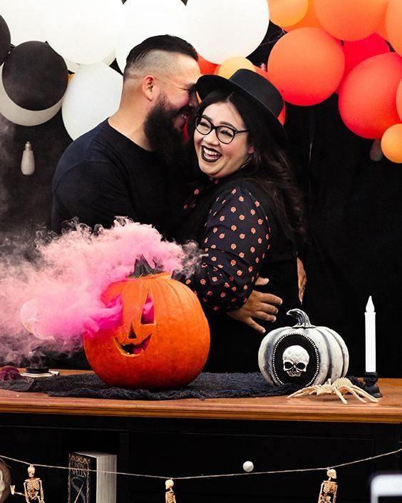 a man and woman standing next to each other in front of a table with halloween decorations