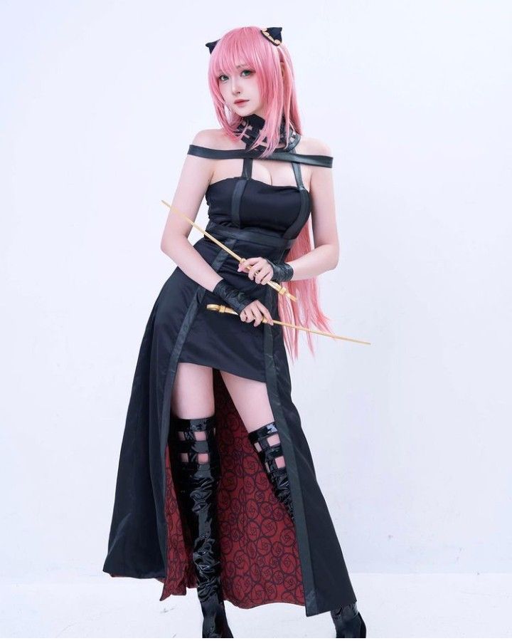 a woman with pink hair is dressed in black and holding a bow while standing against a white wall