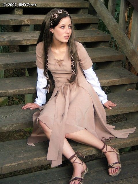 a woman is sitting on some steps wearing a brown dress and holding her hands out