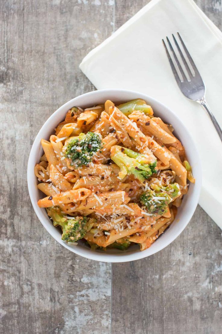 a white bowl filled with pasta and broccoli on top of a wooden table