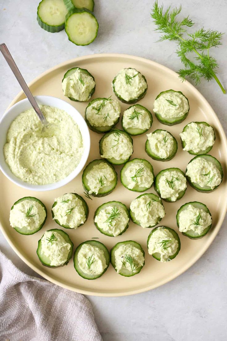 cucumber bites are arranged on a plate with a bowl of dip